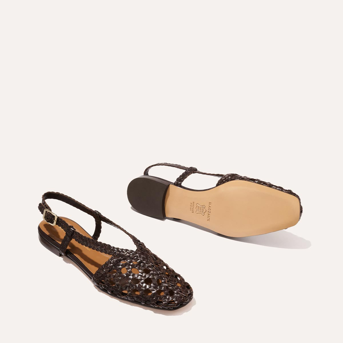 The Altea - Espresso Woven Leather by Margaux features slingback flats with closed, pointed toes in dark brown woven leather. One shoe stands upright, highlighting the pattern; the other lies on its side to show the smooth tan sole—ideal for summer.