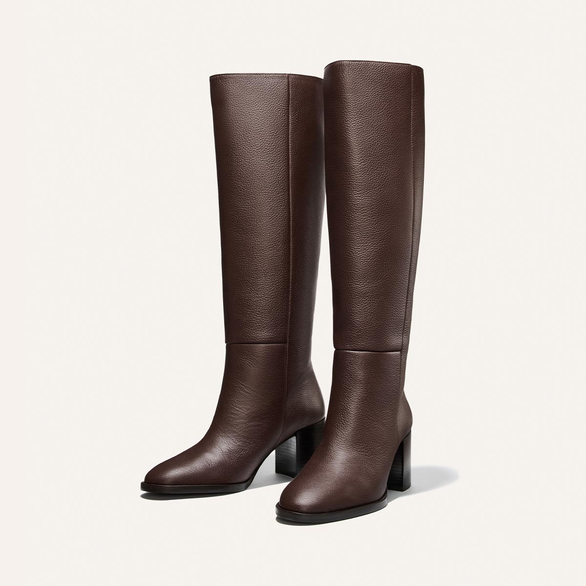 Step into sophistication with the Alison Roman x Margaux: The Charlie Boot in Brown Tumbled Calf—a pair of tall, dark brown leather boots from Margaux featuring rounded toes and high block heels. Displayed against a white background, these are the statement boots your closet can’t be without.