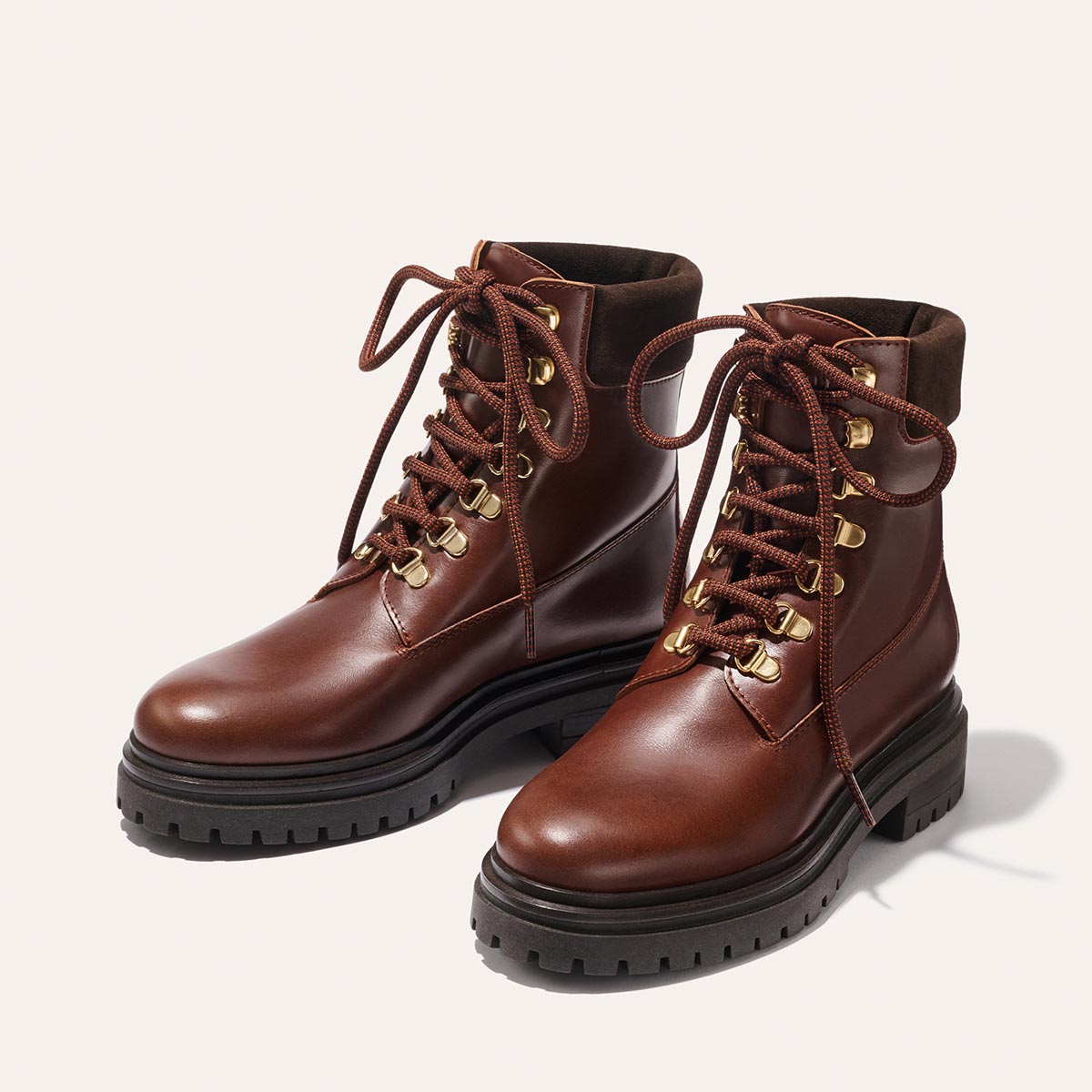 The Aspen Boot - Russet Calf by margaux-development features brown leather, lace-up design, chunky black rubber soles, gold eyelets, and padded ankles, shown on a light background.