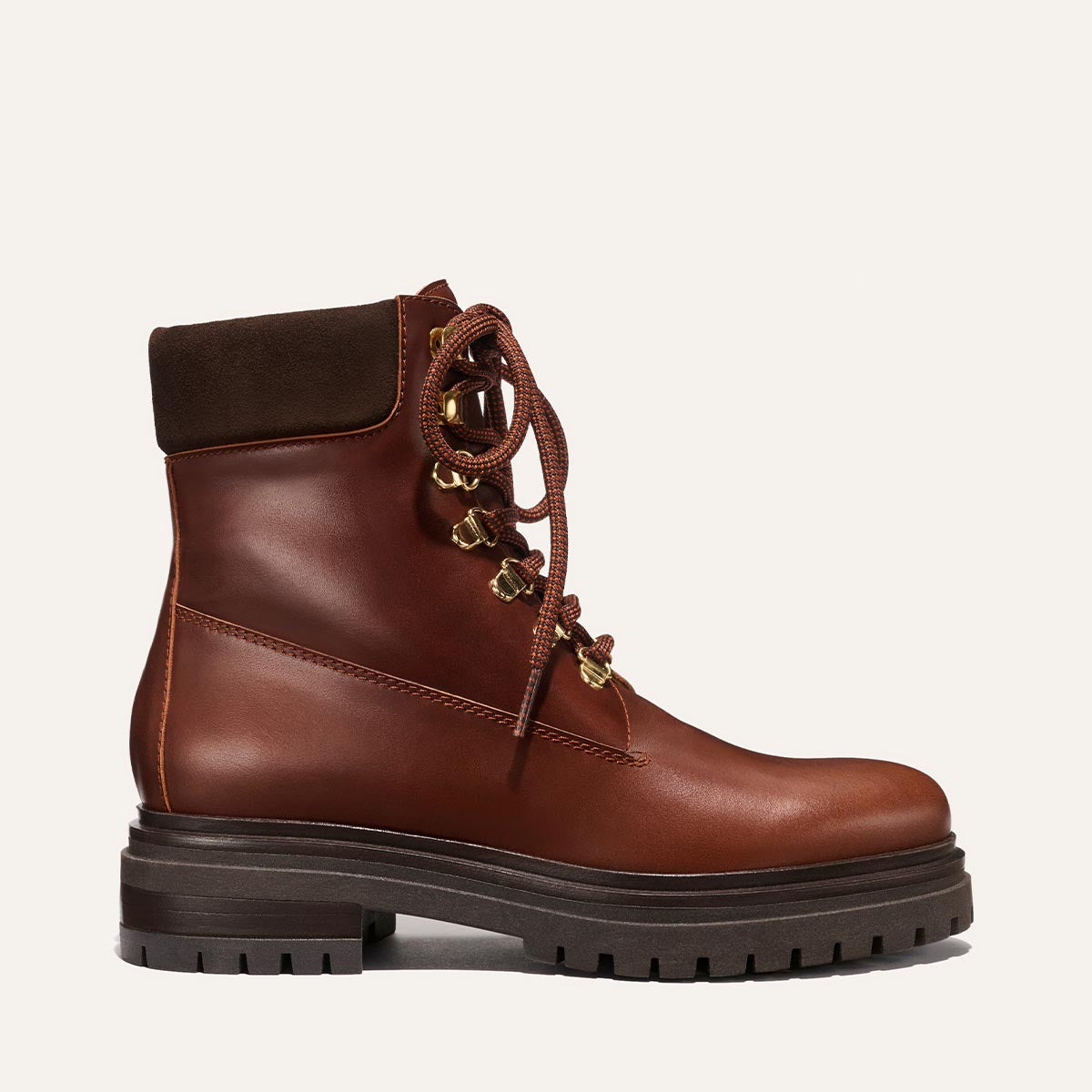 The Aspen Boot - Russet Calf by margaux-development features brown leather, a dark brown padded collar, gold eyelets, and a thick black lug sole. Shown from the side on a plain light background—an all-around-town boot with heritage hiking style.