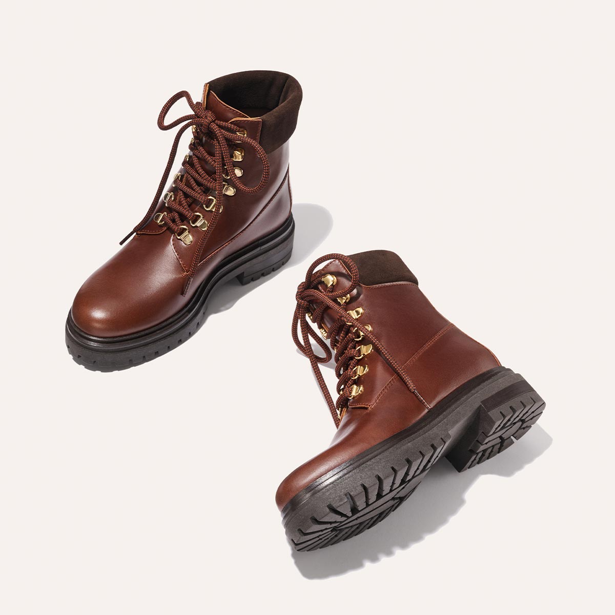 The Aspen Boot - Russet Calf by margaux-development: brown leather lace-up boots with black soles and gold eyelets, shown on a light background—one upright, one on its side to display the textured sole.