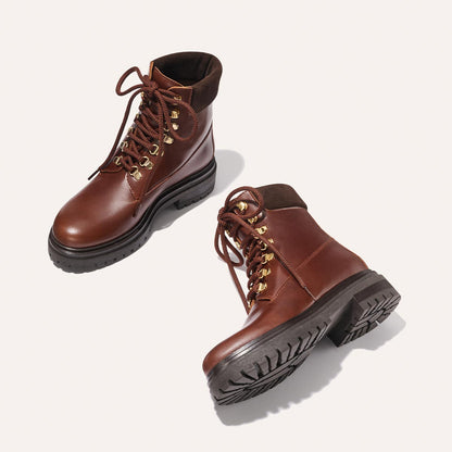 The Aspen Boot - Russet Calf by margaux-development: brown leather lace-up boots with black soles and gold eyelets, shown on a light background—one upright, one on its side to display the textured sole.