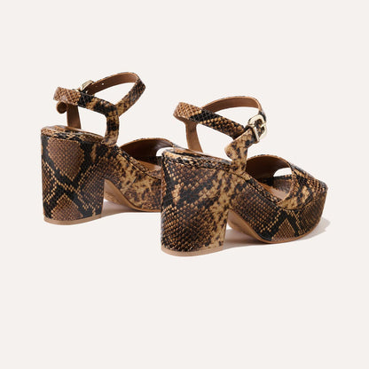The Bardi - Camel Python Embossed by margaux-development features high platform heels, brown and black python-embossed leather, ankle straps with gold buckles, and is showcased against a white background for modern style.