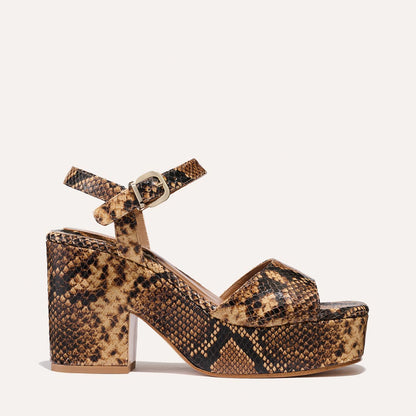 The Bardi by margaux-development is a camel python-embossed chunky-heeled sandal with a thick platform, crisscross toe straps, and an ankle strap with gold buckle—perfect for adding disco glamour to any modern look.