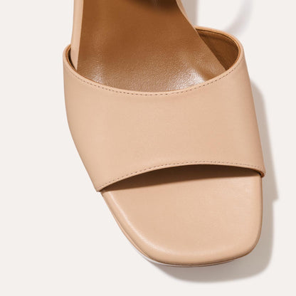Close-up of The Bardi - Petal Calf by margaux-development: a beige open-toe sandal with a wide front strap, square-shaped toe, and modern platform heel, set against a light background.