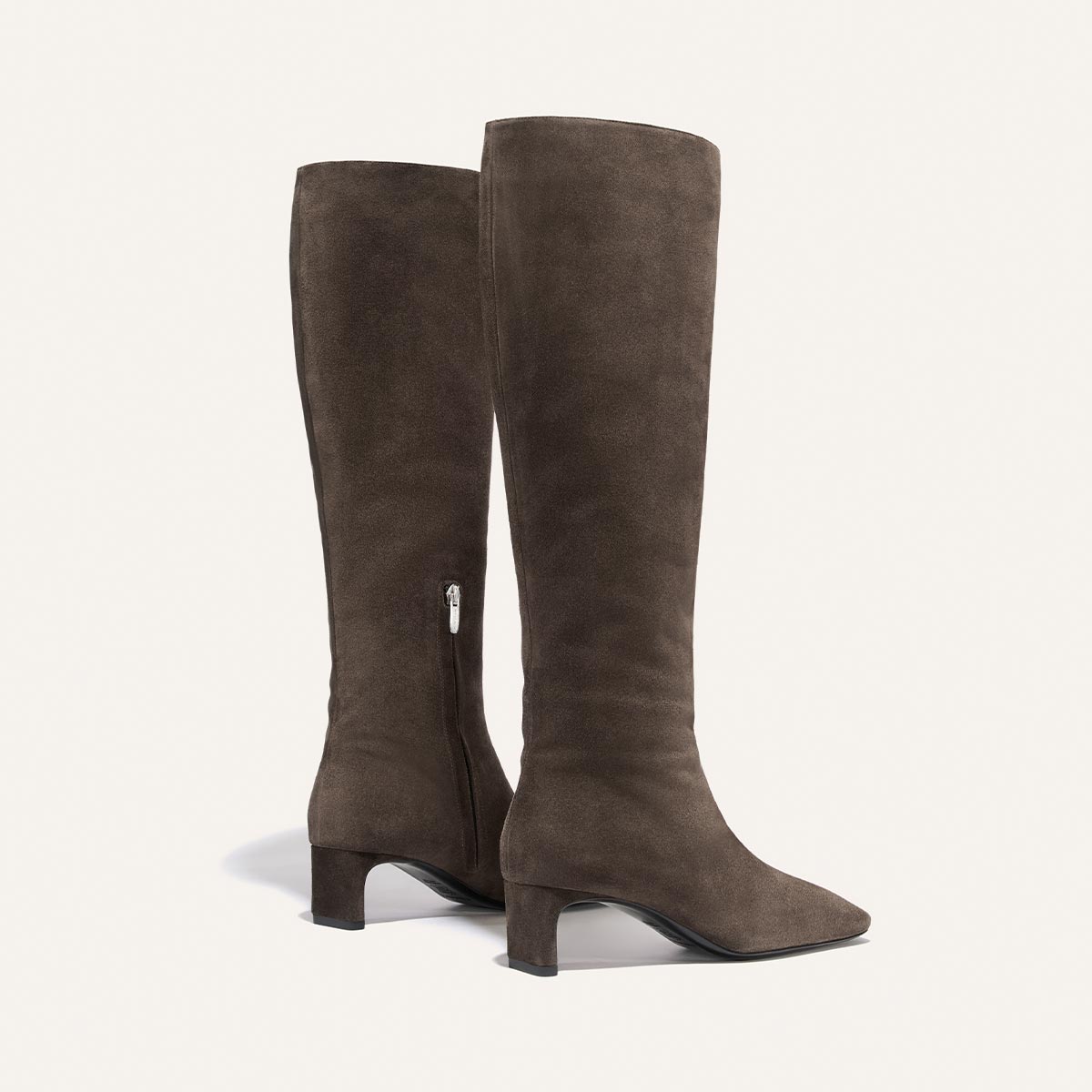 A pair of The Brera Knee-High Boots by Margaux in English Brown Suede, featuring low block heels, padded insoles for comfort, and side zippers, positioned upright on a light background.