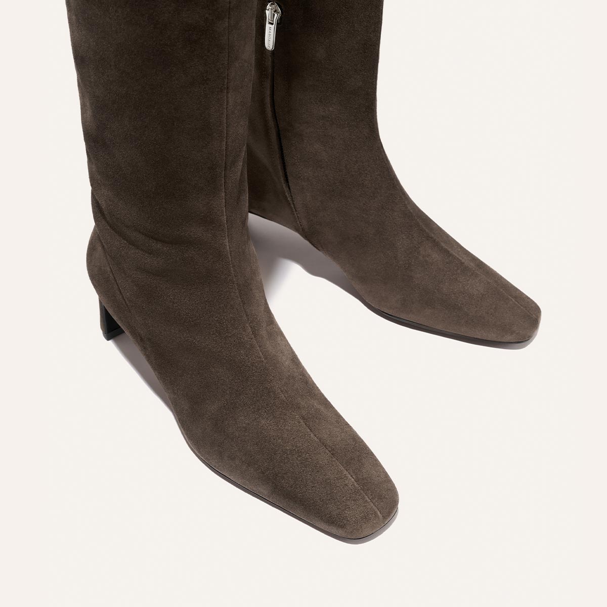 The Brera Knee-High Boot by Margaux in English Brown Suede features a modern square toe, low block heel, and convenient side zipper. This tall boot is designed with a padded insole for all-day comfort and is showcased against a plain light background.