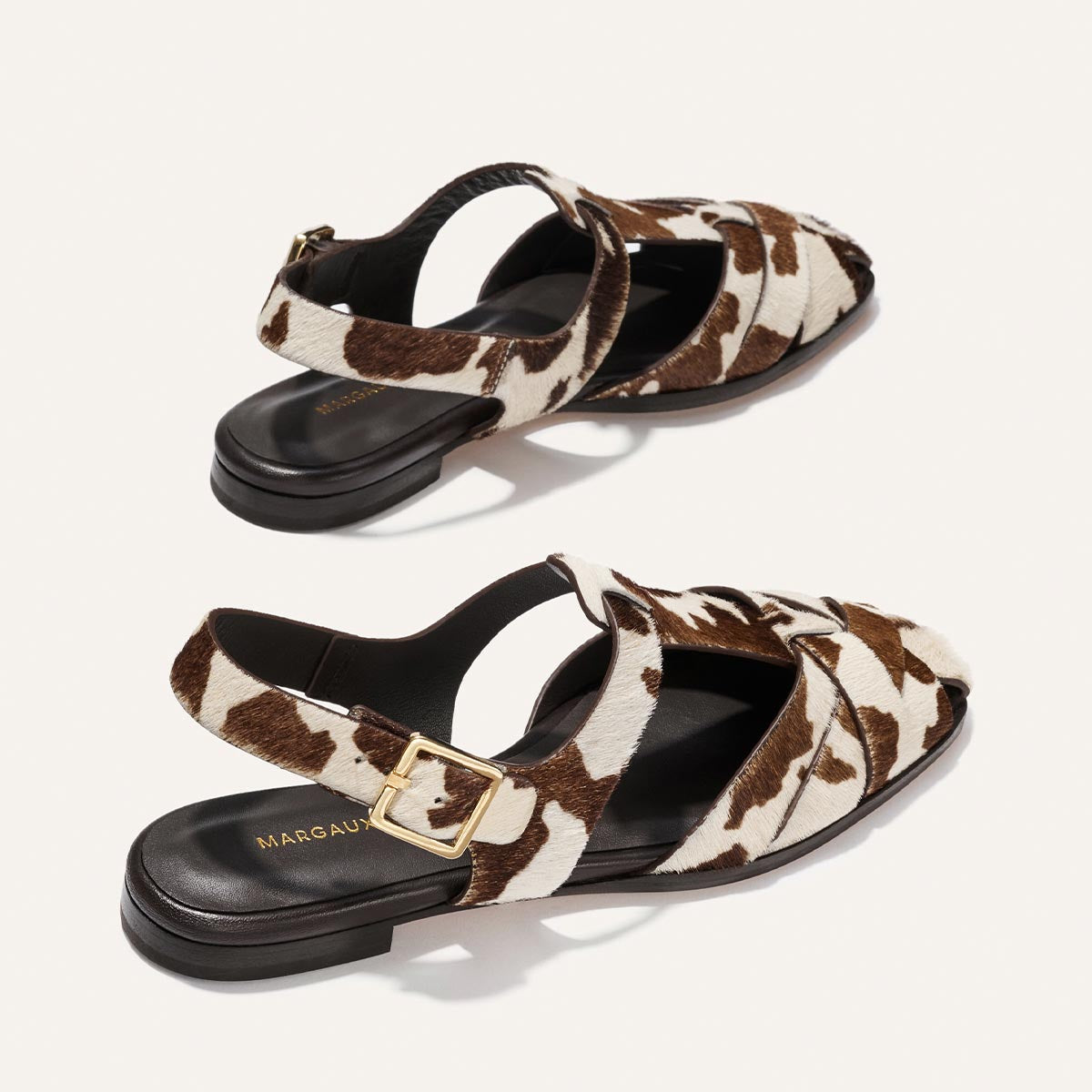 Pair of cow print sandals with a gold buckle on a light background