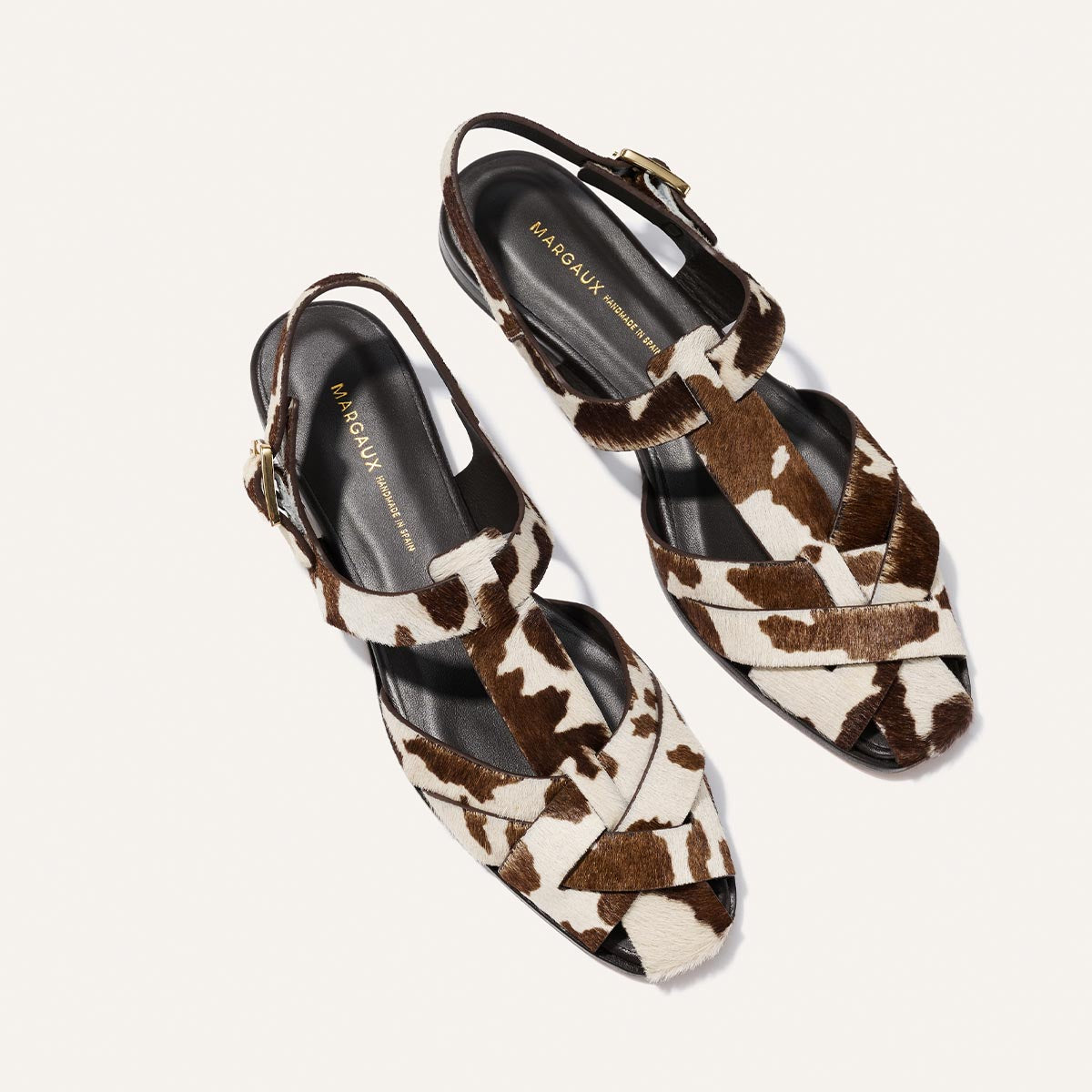 Pair of cow print patterned sandals on a white background