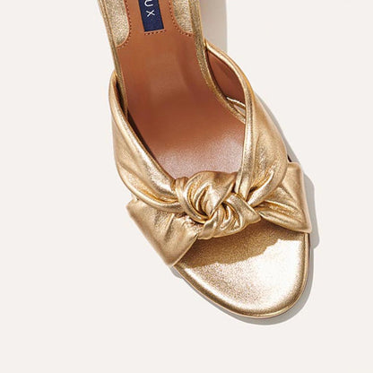 The Carmine Mule in shiny Gold Nappa, a slide-on heel featuring a plush knot detail and comfortable 2.5-inch block heel
