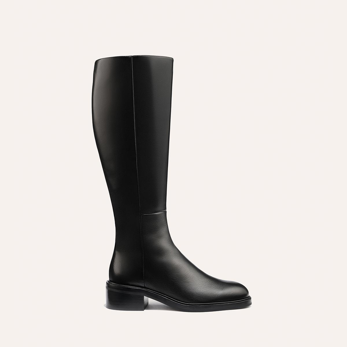 The Margaux City Boot - Black Calf features a tall, black leather knee-high design with a low heel and round toe, offering a sleek, minimal look that channels the classic riding boot silhouette. Displayed against a plain light background.