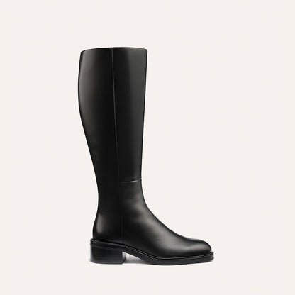 The Margaux City Boot - Black Calf features a tall, black leather knee-high design with a low heel and round toe, offering a sleek, minimal look that channels the classic riding boot silhouette. Displayed against a plain light background.