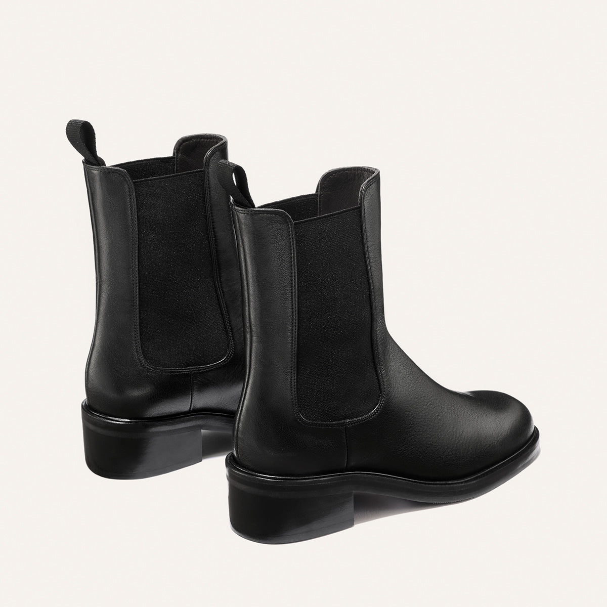 A pair of Margaux’s The City Chelsea Boot - Black Calf, crafted in black leather with elastic side panels and pull tabs, displayed from a rear and side angle against a light background.