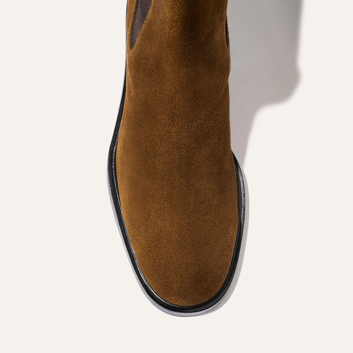 Top view of The City Chelsea Boot - Cedar Suede by Margaux, featuring brown suede and a black sole, displayed on a plain white background. The shadow falls to the right side of the boot.