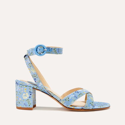 The City Sandal - Blue Floral Satin by margaux-development features a cushioned insole, ankle strap with round buckle, crisscross toe straps, and a vibrant yellow, blue, and white floral pattern on its satin straps and block heel.