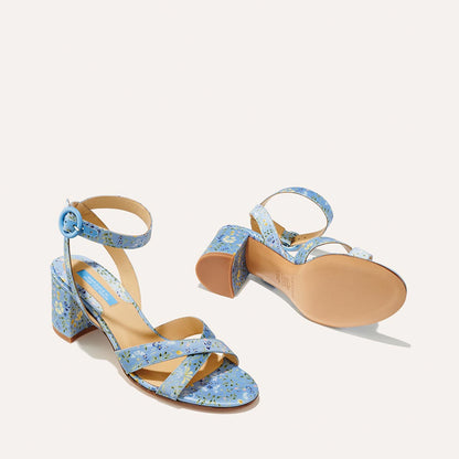 The City Sandal - Blue Floral Satin by margaux-development features blue strappy block heels with a floral pattern, ankle straps with round blue buckles, and tan cushioned insoles, shown on a light background.