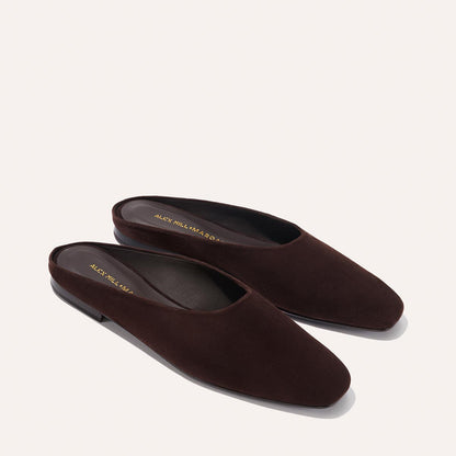 The Margaux Alex Mill x Margaux: The Clara - Espresso Suede mules feature a slipper-like silhouette, closed rounded toes, and flat black soles, shown on a light beige background.