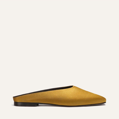 The Clara - Ochre Satin by Margaux: a mustard yellow slip-on mule with a closed toe and black flat sole, shown in profile against a plain light background.