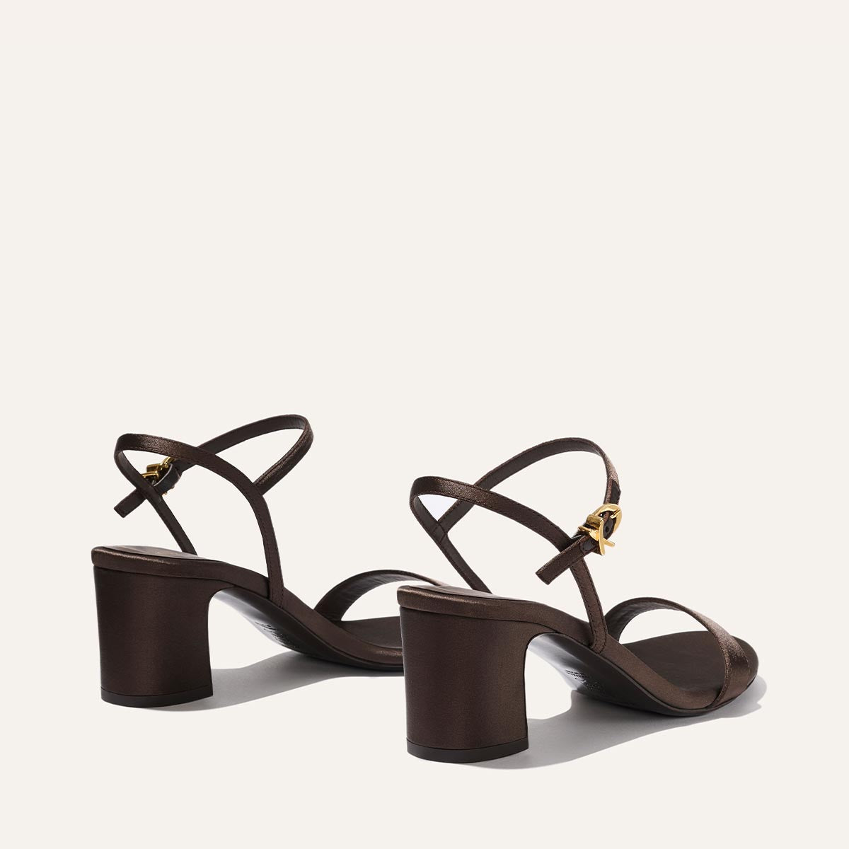 The Cleo Sandal - Espresso Satin by Margaux features brown satin, open toes, mid-height block heels, thin straps, and gold buckle closures, displayed against a plain light background.