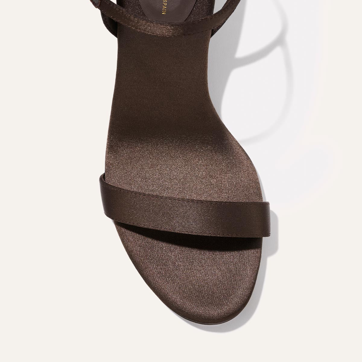 A close-up top view of The Cleo Sandal in Espresso Satin by Margaux, featuring a single toe strap and an ankle strap, displayed against a plain light background.