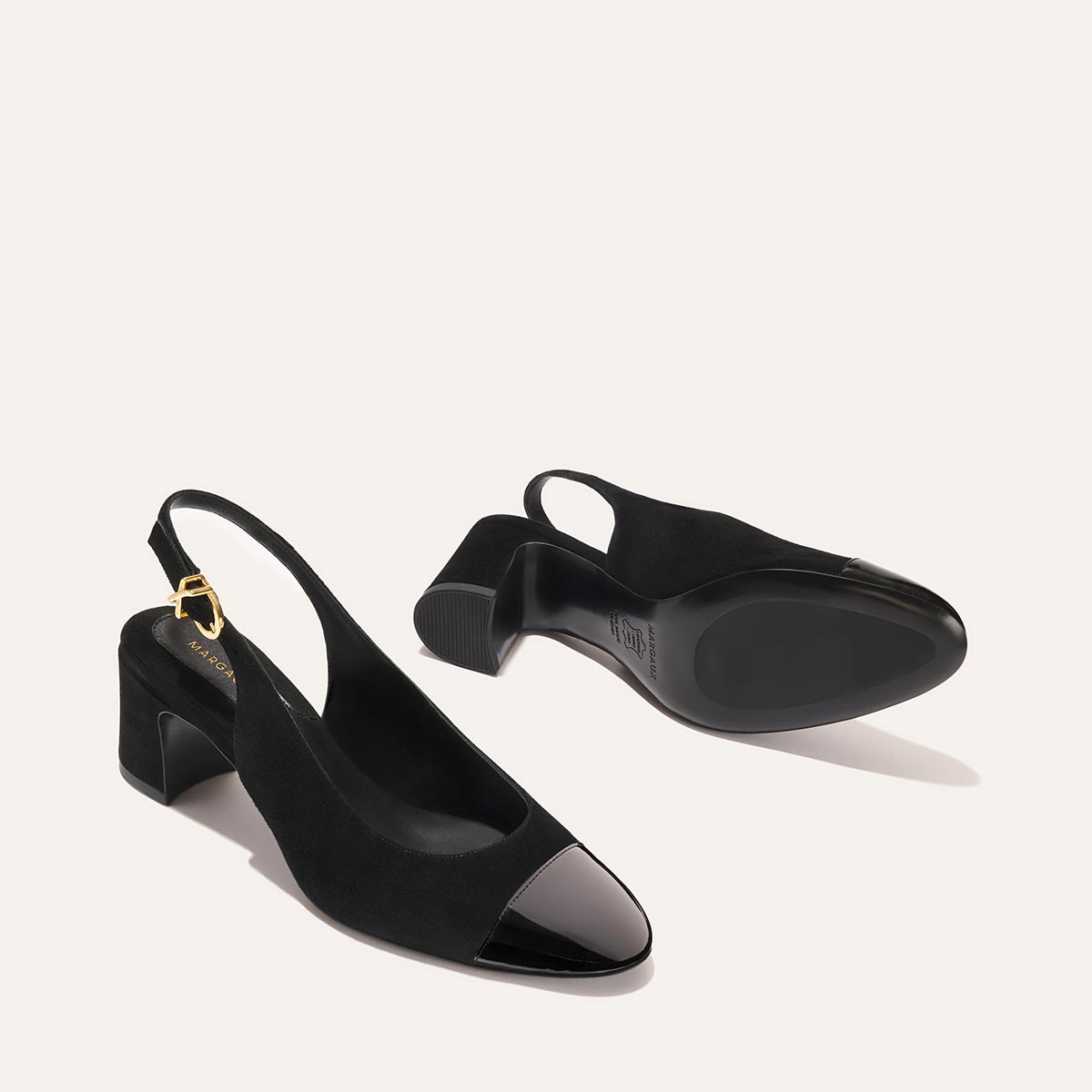 The Cluny Slingback by Margaux in black suede and patent features a pointed toe, glossy cap, and low block heel—perfect as elegant heels or chic work shoes. One shoe is upright; the other shows its sole for a complete view.