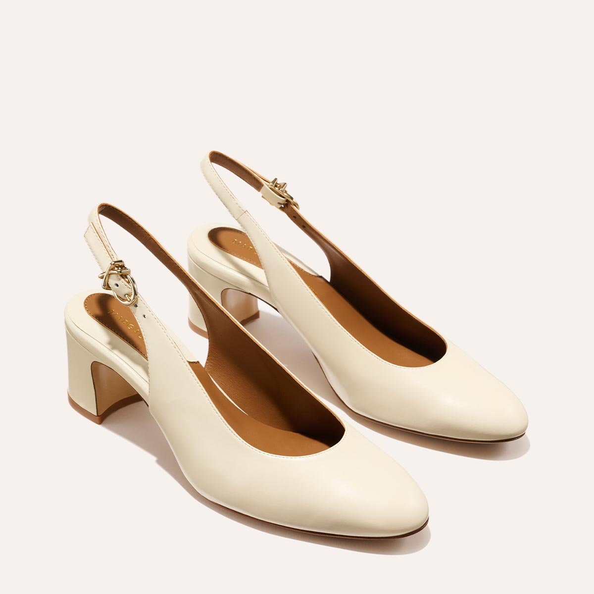 The Cluny Slingback in Cream Nappa, featuring a sleek Italian nappa leather upper with an adjustable buckle and a comfortable 2.5-inch black heel.