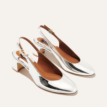 The Cluny Slingback - Silver Mirror by Margaux features shiny silver slingback pump heels with a low block heel, almond toe, buckle strap, and tan insoles—blending Parisian elegance with New York style.