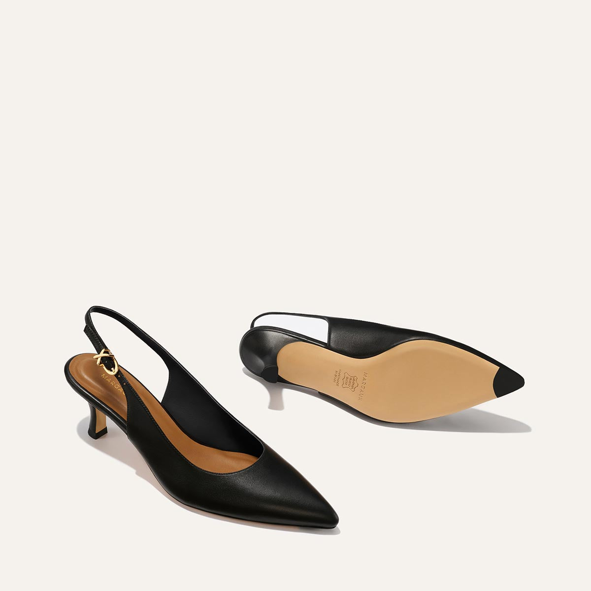 The Colette - Black Nappa by margaux-development features black slingback heels with micro heels, pointed toes, gold ankle buckle, tan insoles. One shoe stands upright; the other shows its beige sole with a black tip.