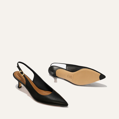 The Colette - Black Nappa by margaux-development features black slingback heels with micro heels, pointed toes, gold ankle buckle, tan insoles. One shoe stands upright; the other shows its beige sole with a black tip.