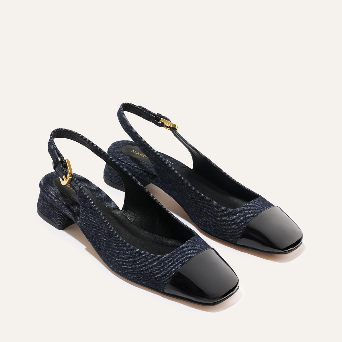 The Darcy Slingback by Margaux features indigo denim fabric, black patent leather square toes, low block heels, and adjustable straps—perfect ballet pumps for warm-weather looks. Displayed on a light background.