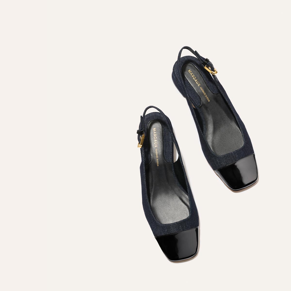 The Darcy Slingback by Margaux in Indigo Denim and Patent features adjustable straps, square toes, and gold buckles—displayed on a light beige background. A chic ballet pump perfect for warm-weather days.