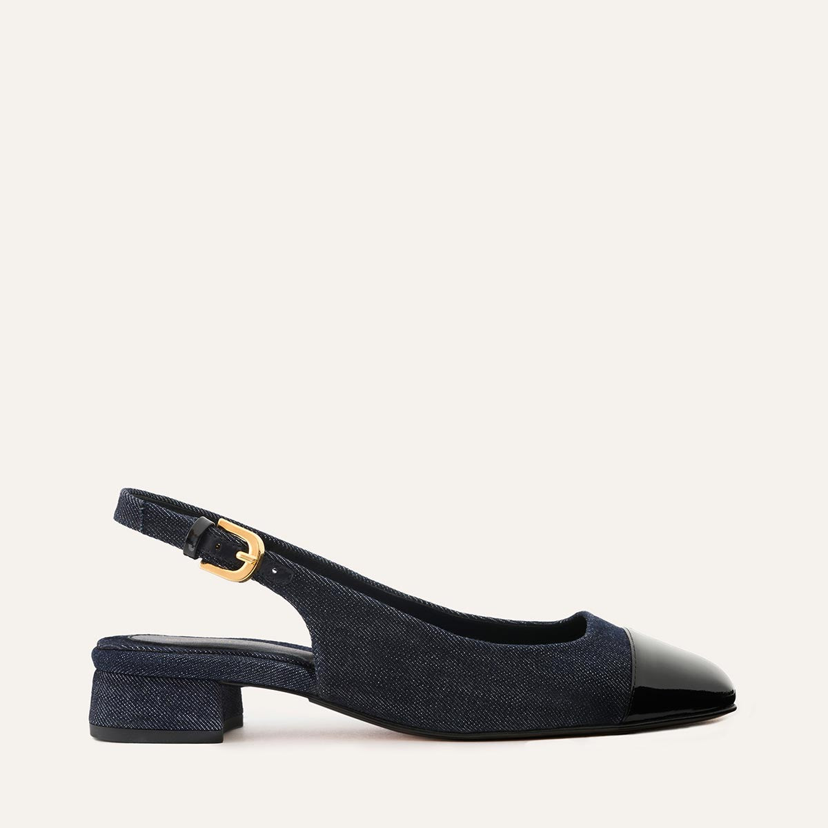 Margauxs The Darcy Slingback in indigo denim and black patent combines a low block heel, gold buckle, and adjustable slingback—all shown in side profile against a light background, ideal for warm-weather style.