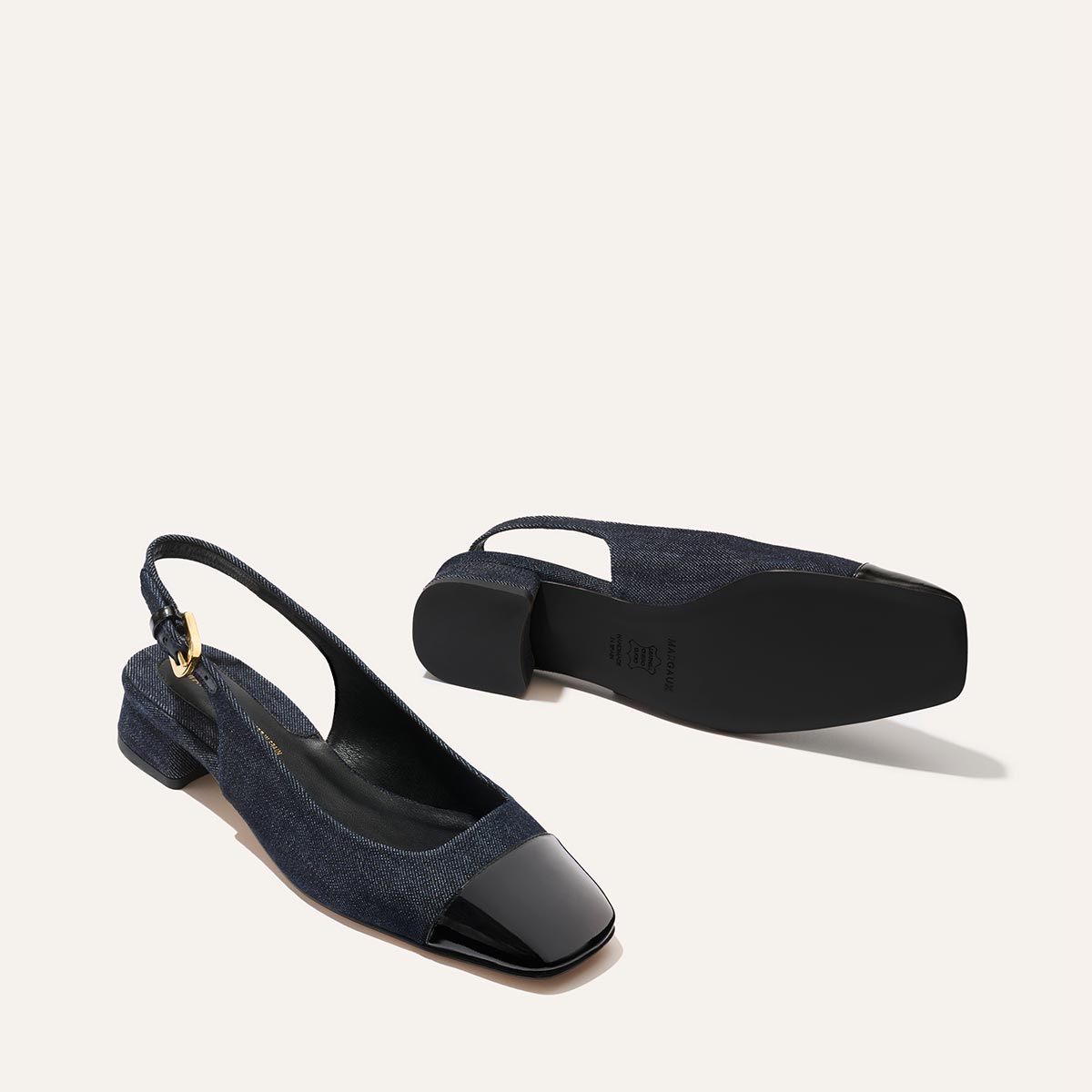 The Darcy Slingback from Margaux features indigo denim uppers, black patent square toes, low block heels, and gold buckle accents. Adjustable slingback design offers chic comfort—perfect for warm weather. Shown on a light background.