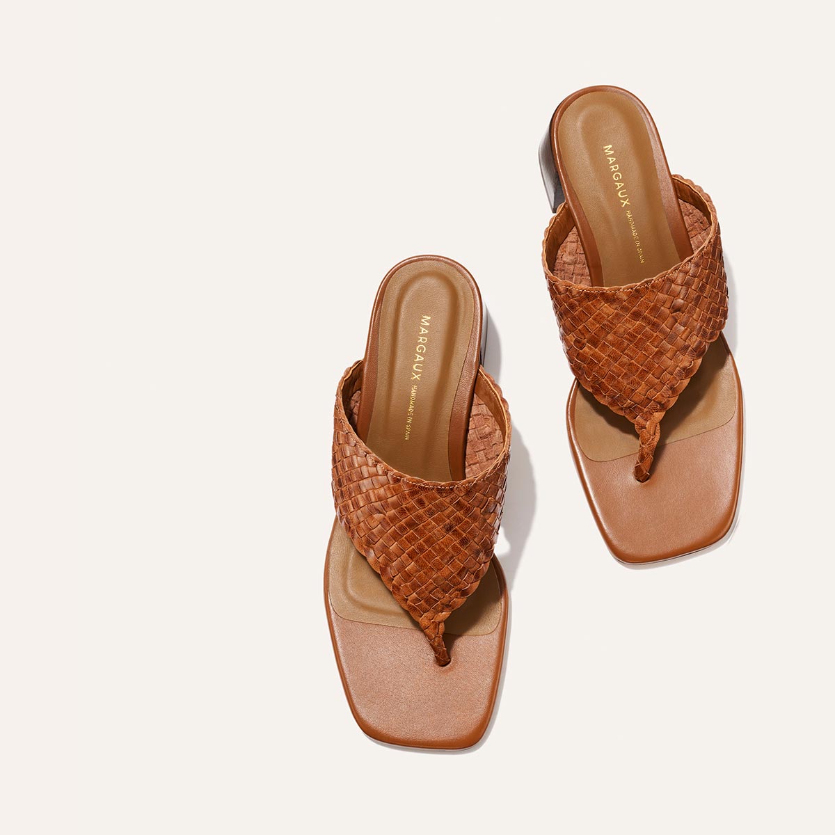 The Deia 50 - Saddle Woven Leather by Margaux: brown woven leather thong sandals with square toes and cushioned footbeds, shown on a light background.