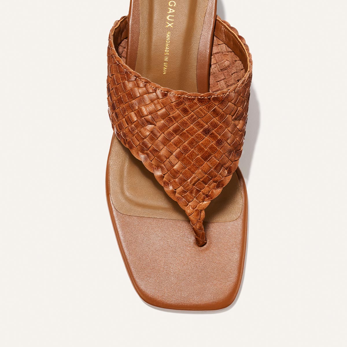 A top view of The Deia 50 - Saddle Woven Leather sandal by Margaux, featuring brown woven leather, a square toe, and thong strap, displayed against a white background.