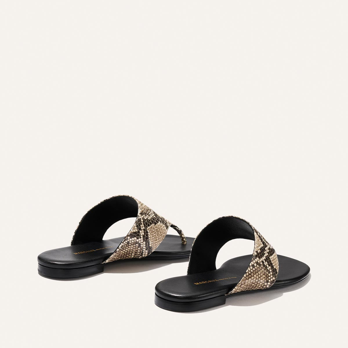 Pair of sandals with snake print straps on a light beige background