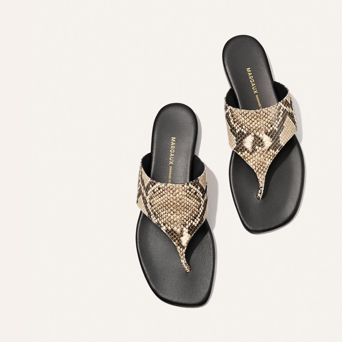 Pair of sandals with snake print straps on a light gray background