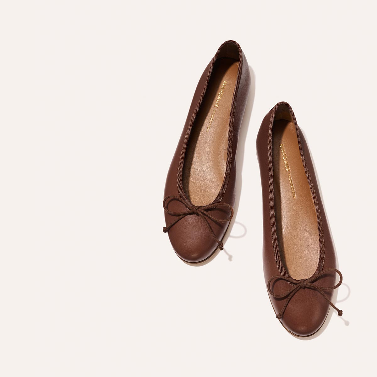 Handmade in Spain, these comfortable brown leather The Demi - Cognac Nappa ballet flats feature a rounded toe and a small bow on the front.