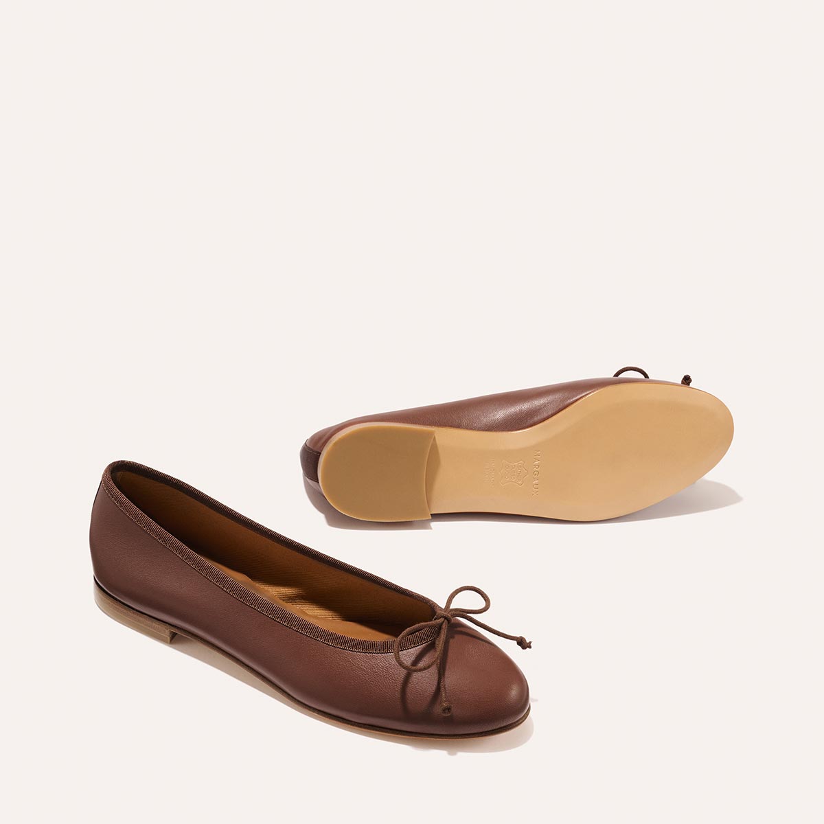 A pair of The Demi - Cognac Nappa leather ballet flats, with one shoe shown from the side and the other from the sole.
