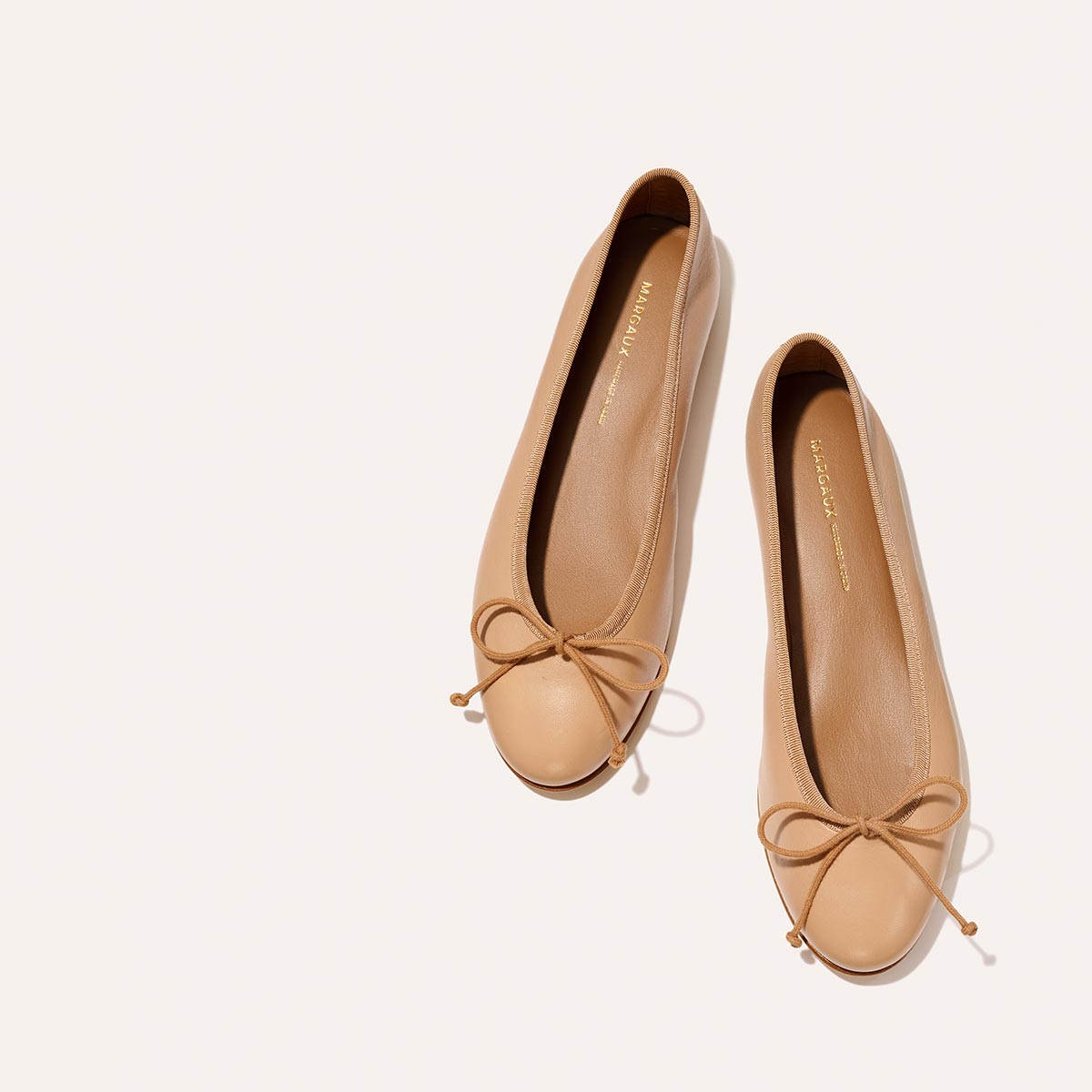 The Demi - Dune Nappa by margaux-development: beige leather ballet flats with rounded toes and small bows, displayed on a light off-white background.