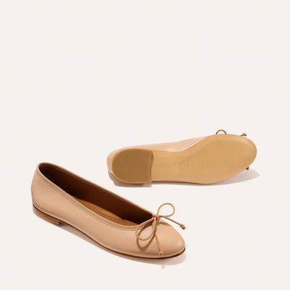 The Demi - Dune Nappa by margaux-development: beige leather ballet flats with rounded toes, small front bows, and flat soles. One shoe stands upright; the other lies on its side displaying the sole.