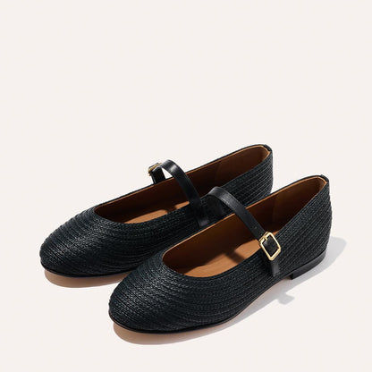 The Demi Jane - Black Raffia by Margaux: black woven Mary Jane flats with rounded toes, tan insoles, and adjustable straps with gold buckles, displayed on a light background.