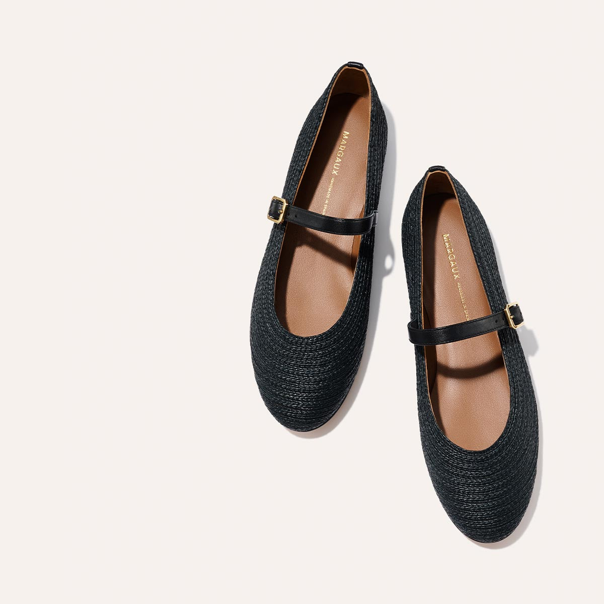 The Demi Jane - Black Raffia by Margaux: black woven Mary Jane flats with brown insoles and gold buckles, shown on a light background.