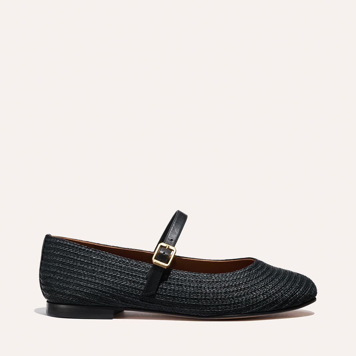 The Demi Jane - Black Raffia by Margaux is a textured Mary Jane flat with a rounded toe, low heel, and slim strap featuring a gold buckle, shown against a plain light background.