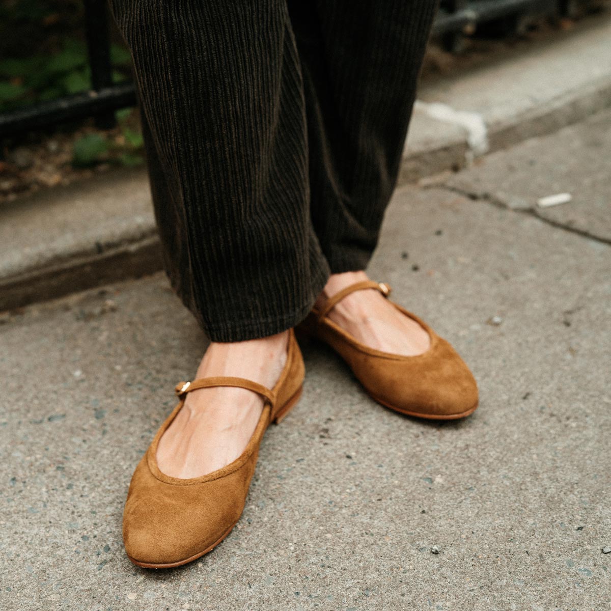 Wearing The Demi Jane - Cedar Suede flats by margaux-development, paired with dark corduroy pants, a person stands on the sidewalk exuding elegant femininity.