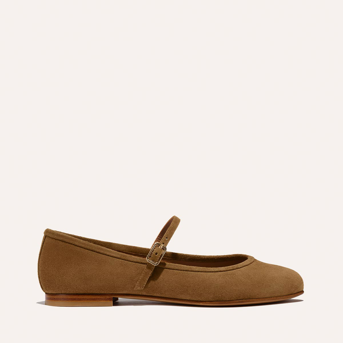 The Demi Jane - Cedar Suede by margaux-development is a tan suede Mary Jane flat with a low heel, round toe, and a single buckle strap, offering elegant femininity against a light background.