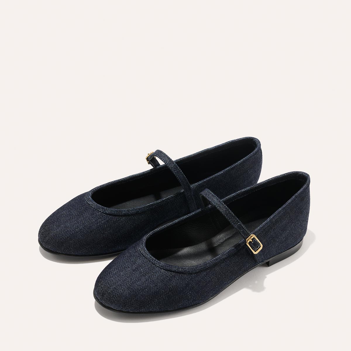 The Demi Jane - Indigo Denim by margaux-development are dark blue flats with rounded toes, low heels, and thin gold-buckled straps, shown on a light background and radiating an elegant, feminine style.