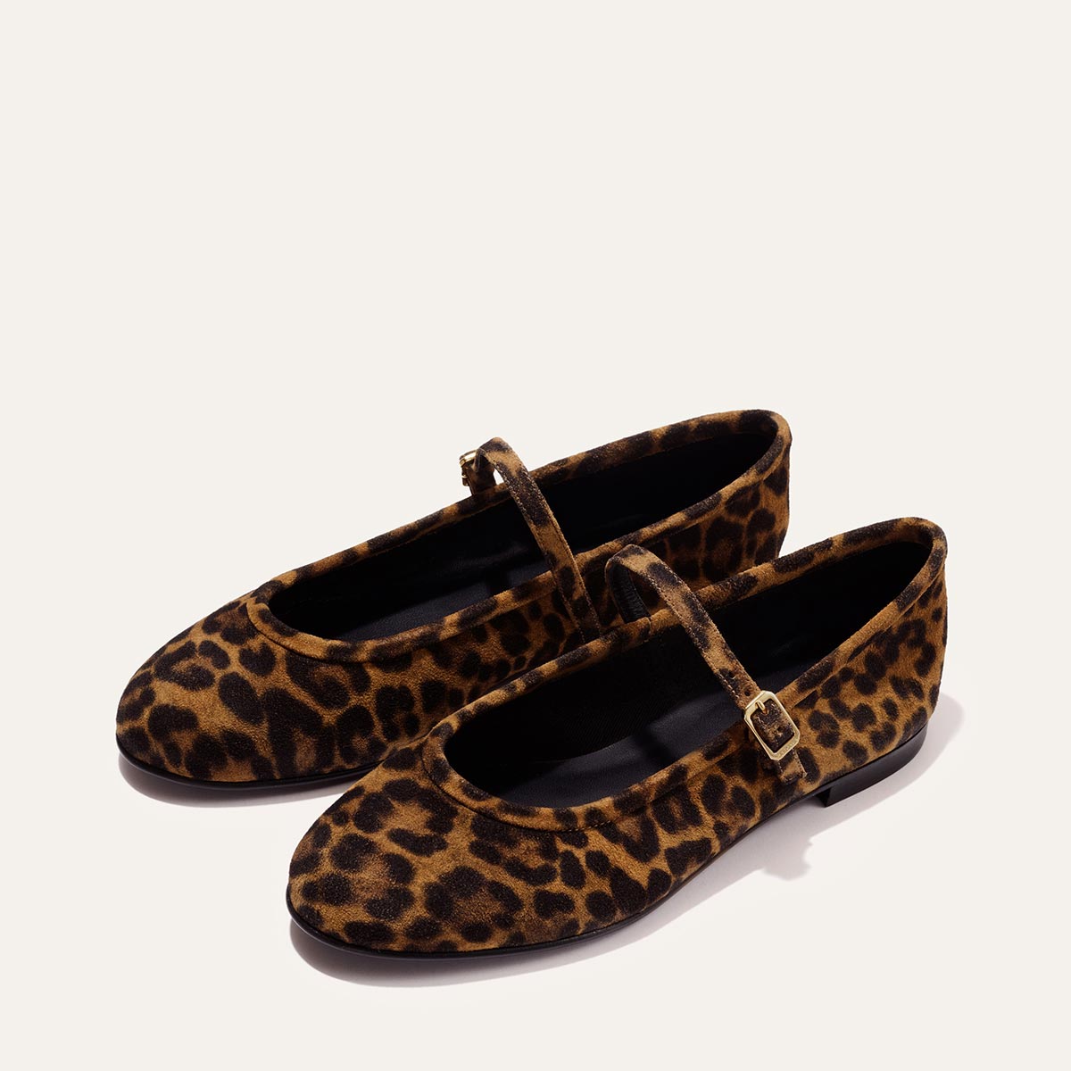 The Demi Jane - Leopard Suede by margaux-development features brown and black leopard print Mary Jane flats with rounded toes, thin straps, and gold buckles, exuding elegant femininity on a light background.