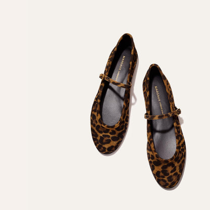 The Demi Jane - Leopard Suede by margaux-development features leopard-print Mary Jane flats with black insoles and thin straps, blending elegance and charm, shown against a light beige background.