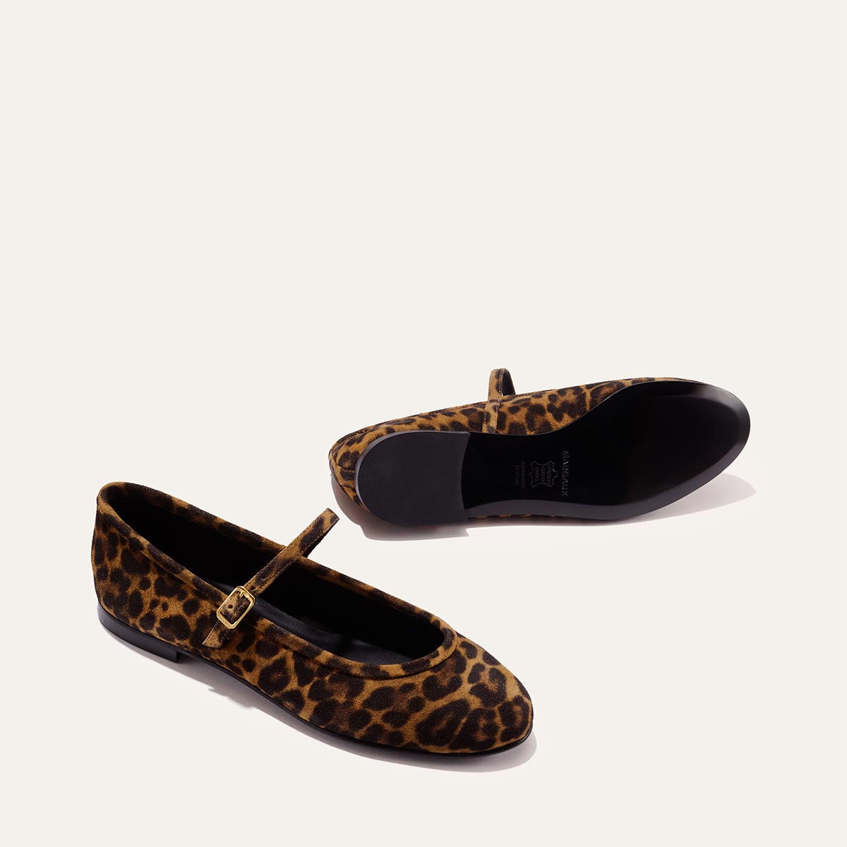 The Demi Jane - Leopard Suede by margaux-development: a pair of leopard suede Mary Jane flats with a gold buckle strap, one upright and one on its side, elegantly displayed on a plain light background.